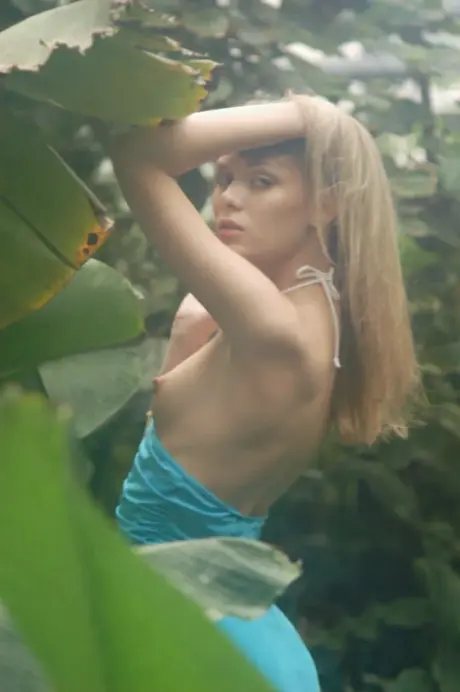 In the lush garden, the blonde woman sheds her dress and goes topless