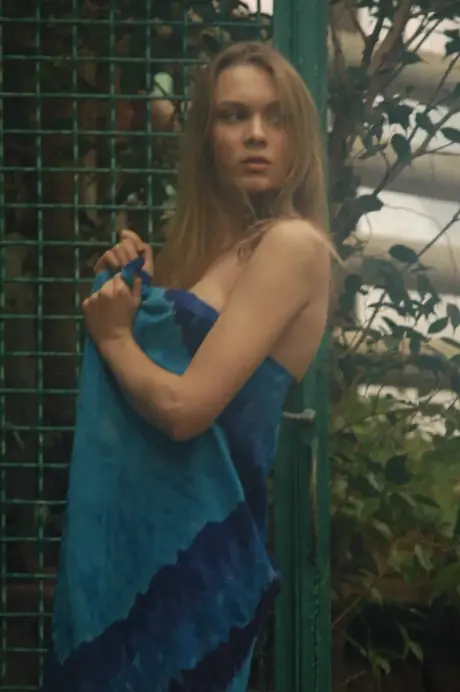 Lush garden scene of a blonde woman removing her dress and going topless