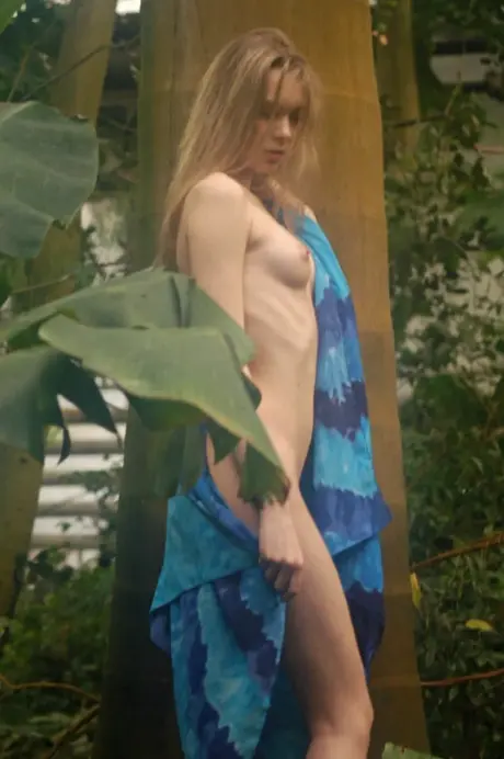 The blonde woman removes her dress, topless in the lush garden