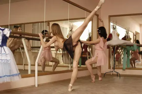 At the barre, stretching ballerinas bare their small breasts