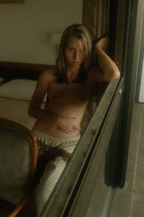 A young woman on her bed enjoys a soft drink before removing all her clothes