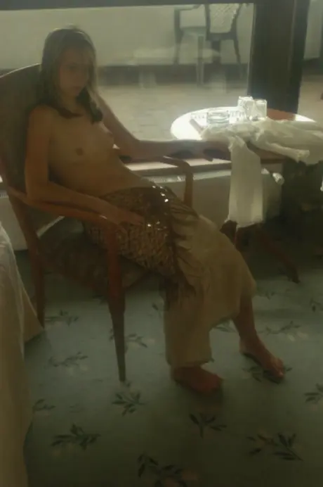 On her bed, a young woman has a soft drink and then undresses completely