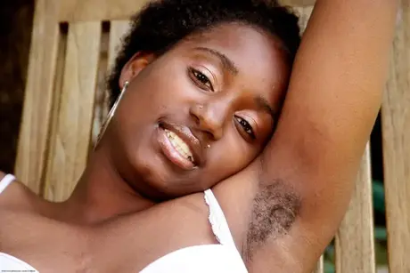 Een ebbenhouten vrouw onthult haar natuurlijke kutje terwijl ze op een tuinstoel zit