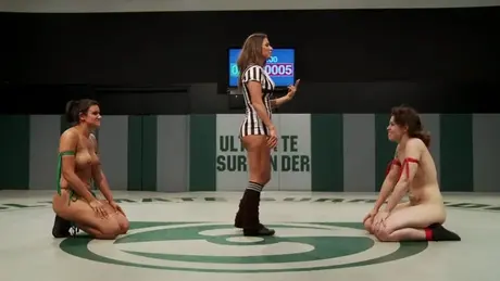 マットの上で縛られたレズビアンのレスラーをからかうレフェリー