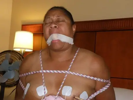 Gefesselte und geknebelte dunkelhäutige BBW erträgt Stromschläge auf einem Bett