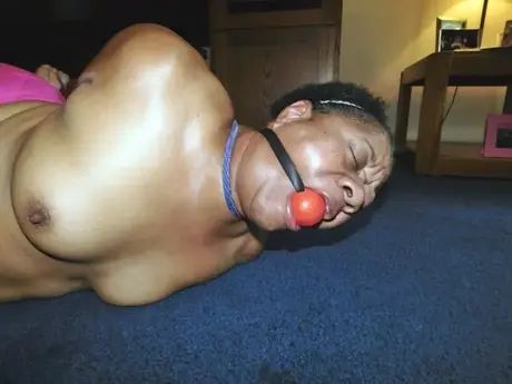 Trixie, en overvægtig sort kvinde, kæmper i en hogtie, mens hun bærer en boldgag