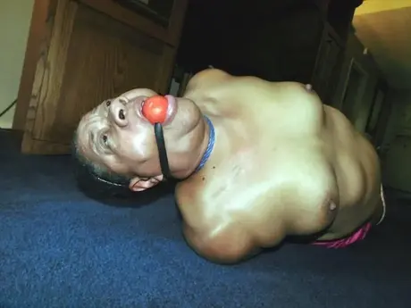 Trixie, en overvægtig sort kvinde, kæmper i en hogtie, mens hun bærer en boldgag