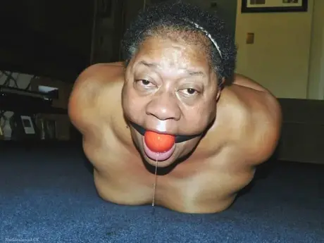 Trixie, en overvægtig sort kvinde, kæmper i en hogtie, mens hun bærer en boldgag