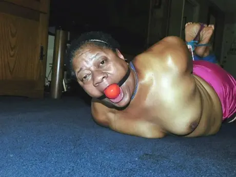 Trixie, en overvægtig sort kvinde, kæmper i en hogtie, mens hun bærer en boldgag