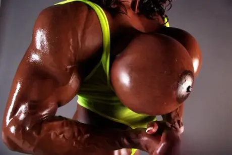 Yvette Bova, den mørkhudede bodybuilder, afslører sine enorme bryster under en vægtløftningssession