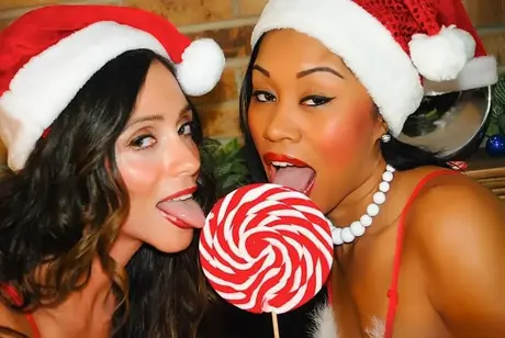 Lesbianas interraciales se complacen mutuamente junto a la repisa de la chimenea con atuendos navideños