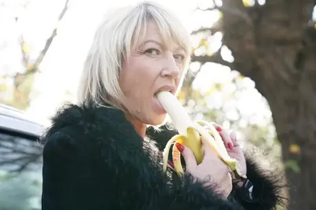 Moden blond kvinde spiser en banan før en gangbang på landet