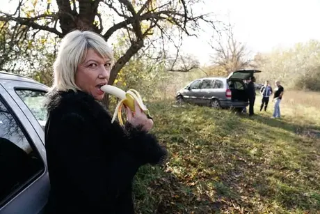 Moden blond kvinde spiser en banan før en gangbang på landet