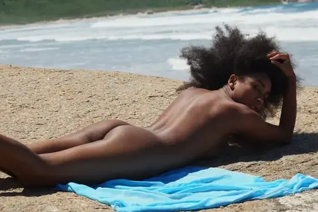 Isadora, ibenholtglamourmodellen, poserer nøgen ved havet med voluminøst stort hår