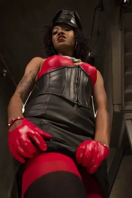 Lotus Lain, ebony femdom v kůži, ukazuje svá malá prsa a bradavky