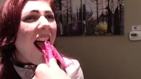 Zrzavá studentka s růžovými kolíčky na prádlo na jazyku a obojkem