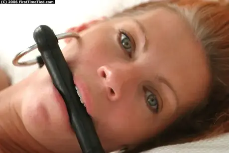 Modelo amateur atada a una cama con una mordaza de freno de caballo, desnuda