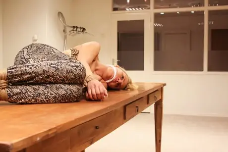 Bundet og kneblet på et bord kæmper den blonde Adrienne for at komme fri