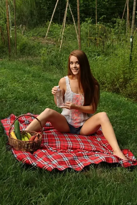 Una belleza pelirroja se desnuda sobre una manta mientras pela un pepino