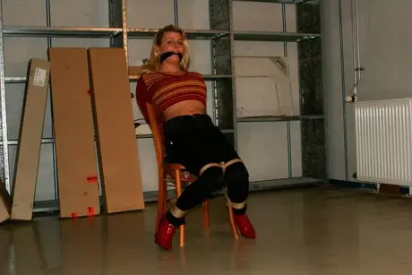 La magnifique blonde Adrienne attachée à une chaise en crop top et jean serré