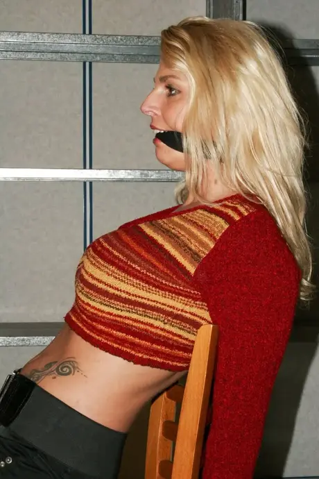 La magnifique blonde Adrienne attachée à une chaise en crop top et jean serré