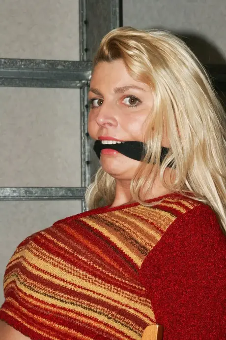 La magnifique blonde Adrienne attachée à une chaise en crop top et jean serré