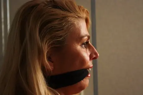 La magnifique blonde Adrienne attachée à une chaise en crop top et jean serré