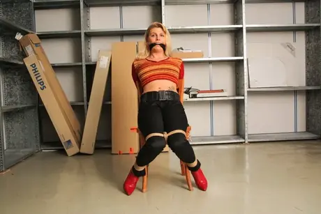 La magnifique blonde Adrienne attachée à une chaise en crop top et jean serré