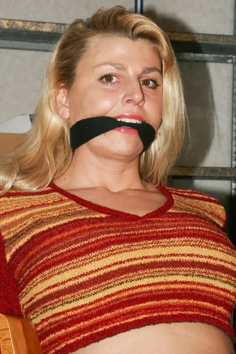 La magnifique blonde Adrienne attachée à une chaise en crop top et jean serré