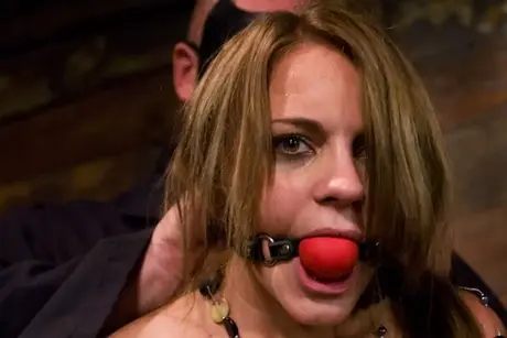 Kirra Lynne, die brünette Sklavin, ist gefesselt, mit einem Ballknebel geknebelt und dominiert