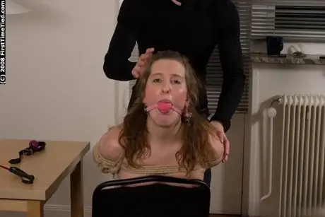 Maskierter Mann beugt eine nackte Amateurin vor, die mit Seil gefesselt und mit Ballknebel geknebelt ist