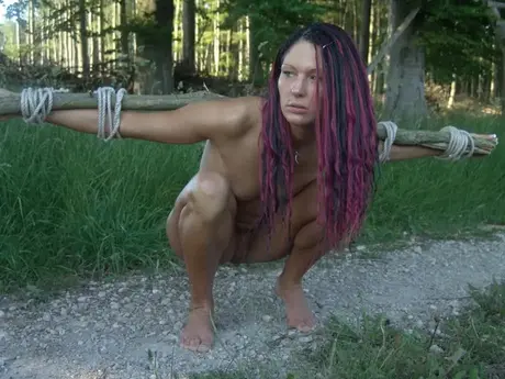 Nackte Frau mit Händen und Handgelenken an eine Holzleiter nahe einer Baumgruppe gefesselt
